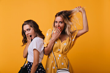 Amazing brown-haired girl expressing surprised emotions while posing with best friend. Caucasian blonde woman having fun with sister during photoshoot.