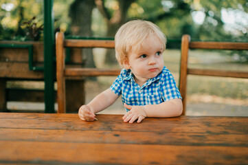 Little cheerful caucasian boy in blue shirt and blue shorts goes for a walk in the park