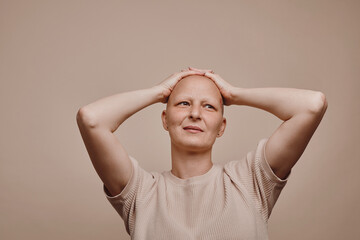 Warm-toned waist up portrait of confident bald woman looking away with hands on head while posing...