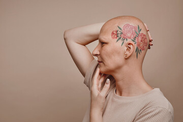 Minimal side view portrait of bald woman with head tattoo posing against beige background in...