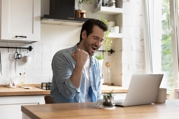 Overjoyed millennial Caucasian guy in glasses look at laptop screen triumph read good news or email on gadget, excited young man feel euphoric win online lottery on computer, luck, success concept