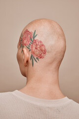 Minimal back view portrait of bald woman with head tattoo posing against beige background in...
