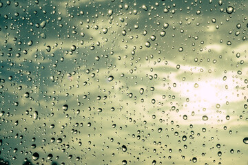 Raindrops on the window with cloudy sky and bursting sun rays in the background 