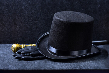 A magician's set: tall hat, leather gloves and a knobbed cane on a black background