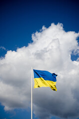 Blue and yellow Ukrainian national flag on a flagpole against a blue sky and white clouds, flag waving in the wind