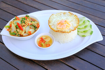 Pad Ka-prao; stir fried chopped chicken with chili and basil, served with steamed rice and fried egg on top set on wooden table