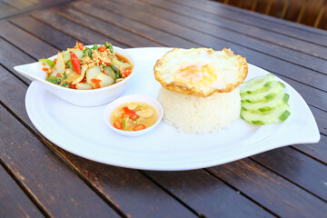 Pad Ka-prao; stir fried chopped chicken with chili and basil, served with steamed rice and fried egg on top set on wooden table