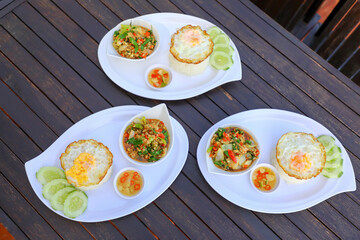 Pad Ka-prao; stir fried chopped chicken with chili and basil, served with steamed rice and fried egg on top set on wooden table