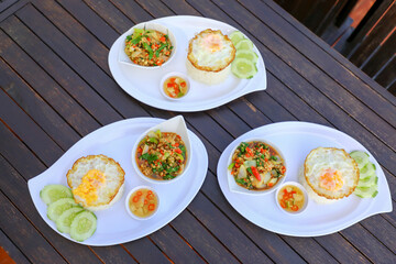 Pad Ka-prao; stir fried chopped chicken with chili and basil, served with steamed rice and fried egg on top set on wooden table