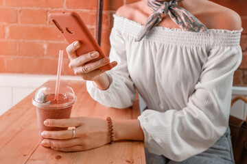 Happy asian girl drinks a smoothie in a cafe and reads the news in social networks on her smartphone.