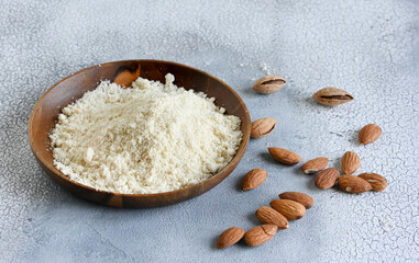 Almond flour in a wooden bowl, almonds on old light background