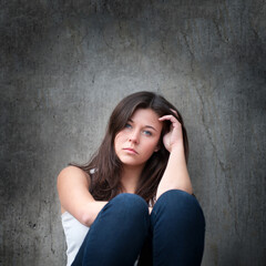 Outdoor portrait of a sad teenage girl looking thoughtful about troubles in front of a dirty gray wall