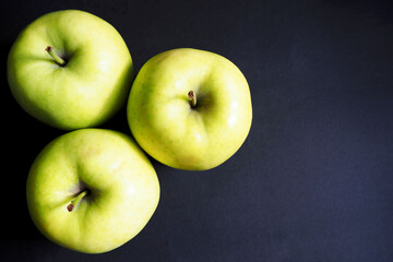 three large green gold apples on a black background top view . organic fruit