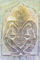 Fototapeta na wymiar Carved Bas Relief of praying man sitting with his legs crossed, in Angkor Wat in Siem Reap, Cambodia