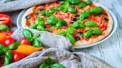 Italian pizza,basil leaves and vegetables on a background of linen fabric, selective focus.
