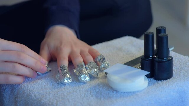 Woman wrapping foil with remover on nails to remove shellac making manicure herself at home. Removing gel Polish from nails, top view.