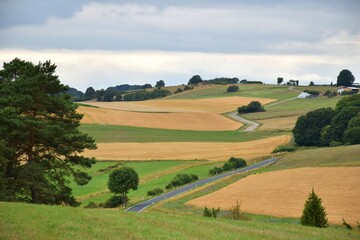 Country road winding through colorful landscape with fields and meadows in Eifel mountains, Germany
