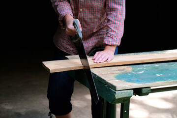 Carpenter woman with handsaw cutting wooden board in workshop. Carpentry, construction, woodworking concept.
