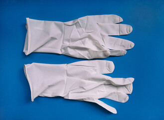 Pair of medical white latex protective gloves on blue background. Protective disposable gloves against the spread of virus, flu, coronavirus (COVID-19), bacterial. Health care and surgical concept.