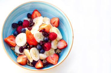 Fresh fruits and berries bowl as a part of healthy breakfast with the copy space on the right of the bowl shoot from the top on the white surface. 