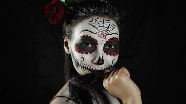 Mexican day of the dead. Young woman with a sugar skull Halloween makeup turns and looks at the camera. Happy Halloween. High quality 4k footage