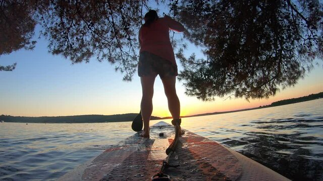 LD Low angle shot of a woman on a SUP paddling towards the sunset