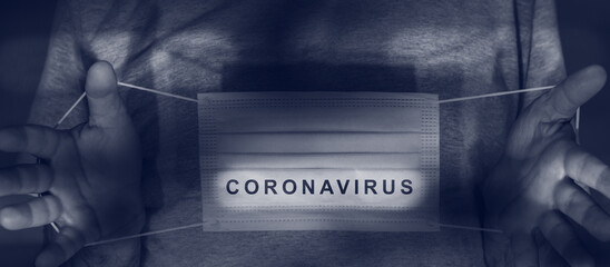 coronavirus word against protective face mask held in the hands,blue shade image