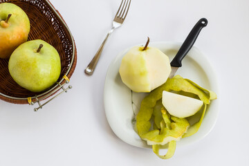 Fresh,peeled pear in plate with knife on white background near basket