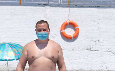 caucasian man in swimming shorts and a protective mask against the background of a white wall with...