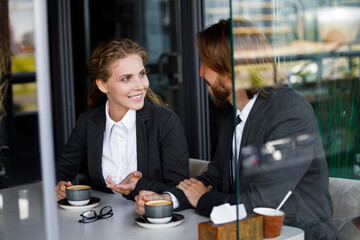 Charming and cute businesswoman with a smile communicates with a partner over a cup of coffee. Young european girl drinks coffee with a partner