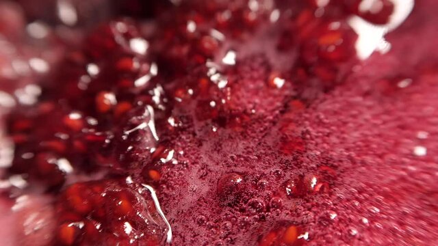 Raspberry jam in the process of boiling. Raspberry syrup. Pink background with bubbling bubbles and raspberries. Procedure for harvesting berries for the winter. Cooking raspberries with sugar. 