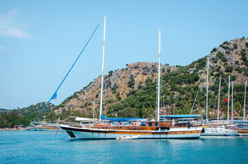 Fototapeta na wymiar Tourist ship on the background of a beautiful summer mountain landscape on the Mediterranean sea. Excursion to Turkey. Sea tour of the historical monument of architecture. People on vacation