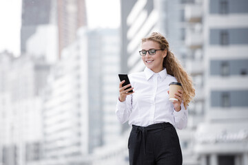 Fototapeta premium Portrait of a smiling european girl woman walking in the city with cellphone