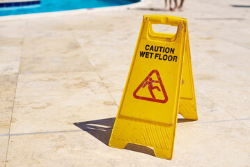 Yellow wet floor caution sign in summer day, closeup