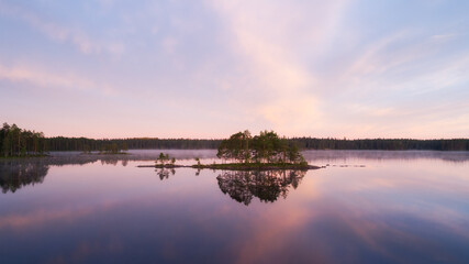 Fototapeta na wymiar Beautiful calm lake with islands. Early misty summer morning with clouds. Pink sunset sky over wild lake. Cloud reflections in water. Nature of Finland. 