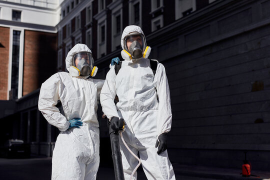 brave professional disinfectors in protective hazmat suit walking through city streets and spraying disinfectant to stop spreading highly contagious coronavirus or COVID-19, use special equipment
