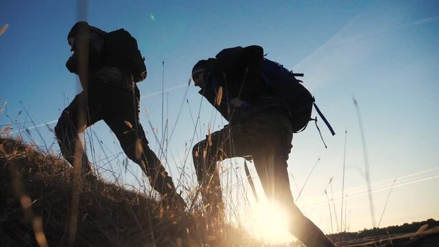 two tourists teamwork with backpacks slow motion walking go silhouette in the sunlight glare of the sun at sunset. two men hikers climb mountains overcoming lifestyle difficulties concept teamwork