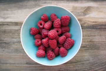 Raspberry close-up in a blue plate on a wooden background. Selective focus