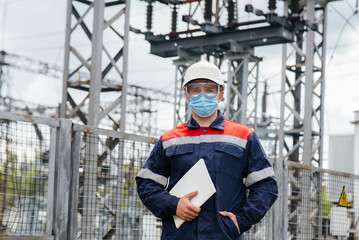 An electrical substation engineer inspects modern high-voltage equipment in a mask at the time of...