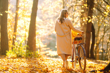 Young smiling girl with a bicycle walks in the autumn forest at sunset.