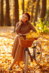 Young smiling girl with a bicycle walks in the autumn forest at sunset.