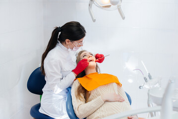 A professional dentist treats and examines the oral cavity of a pregnant girl in a modern dental office. Dentistry