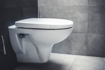 Naklejka na ściany i meble Ceramic white toilet bowl near grey wall, side light in the modern bathroom