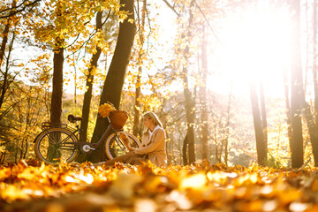 Beautiful young woman sitting on a fallen autumn leaves in a park, reading a book. Smiling girl with a bicycle enjoying rest and freedom. Relaxation and lifestyle concept.