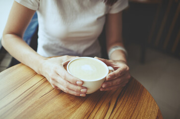 Female hands holding cup of coffee in cafe. Blurred image, selective focus