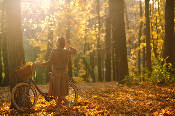 Young girl on a bike in the autumn forest at sunset.