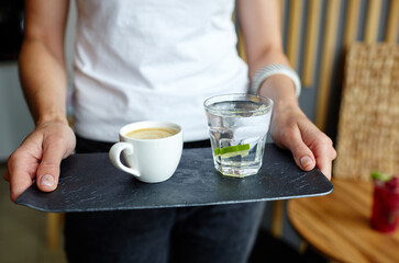 Fototapeta na wymiar Female hands holding stone plate with cup of coffee and water in a glass with lime.Coffee break.Blurred image,selective focus