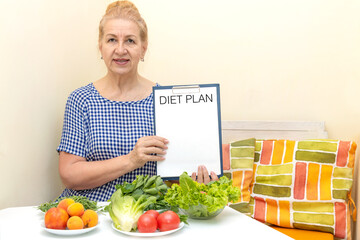 Senior woman is holding a diet plan. Many vegetables and green salad on the table.