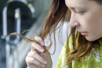 Woman looking at her dry and tangled hair ends.	
