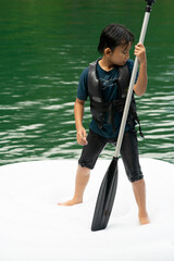 Asian boy wearing life jackets paddling on an inflatable boat in Kenyir Lake, Malaysia.